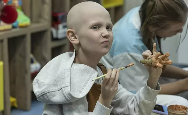 Kira Vertetska, 8, who is undergoing treatment in the oncology department at Okhmatdyt children's hospital in Kyiv, Ukraine, paints a clay figure Thursday Sept. 19, 2024. (AP Photo/Anton Shtuka)