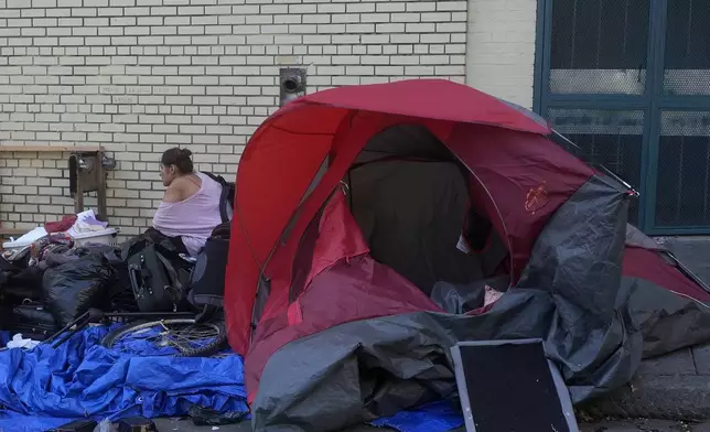 A person sits behind a tent on a sidewalk in San Francisco, Thursday, Aug. 29, 2024. (AP Photo/Jeff Chiu)