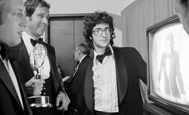 FILE - Chevy Chase, a cast member on "Saturday Night Live," holds his Emmy Award as he watches a monitor showing producer Lorne Michaels accepting another Emmy for the show, while writers Alan Zweibel, left, and Tom Davis, right, look on, during the 28th Primetime Emmy Awards in Los Angeles on May 17, 1976. (AP Photo/Reed Saxon, File)