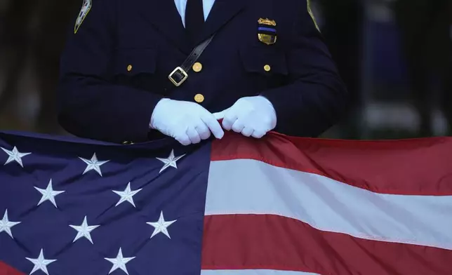 A New Jersey police officer holds an American Flag before the start of the ceremony at the 9/11 Memorial on the 23rd anniversary of the Sept. 11, 2001 terror attacks, Wednesday, Sept. 11, 2024, in New York. (AP Photo/Pamela Smith)