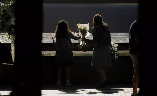 People place flowers on the bronze parapets that ring the reflecting pools during the 9/11 Memorial ceremony on the 23rd anniversary of the Sept. 11, 2001 terror attacks, Wednesday, Sept. 11, 2024, in New York. (AP Photo/Pamela Smith)