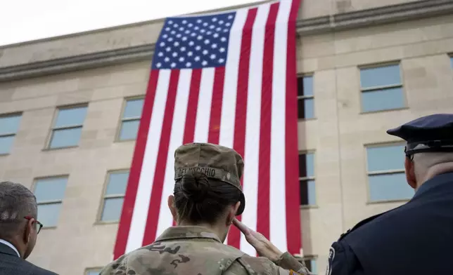 Members of the military and first responders salute as a flag in unfurled from the top of the Pentagon during a dawn Sept. 11th remembrance ceremony on Wednesday, Sept. 11, 2024 in Washington. (AP Photo/Kevin Wolf)