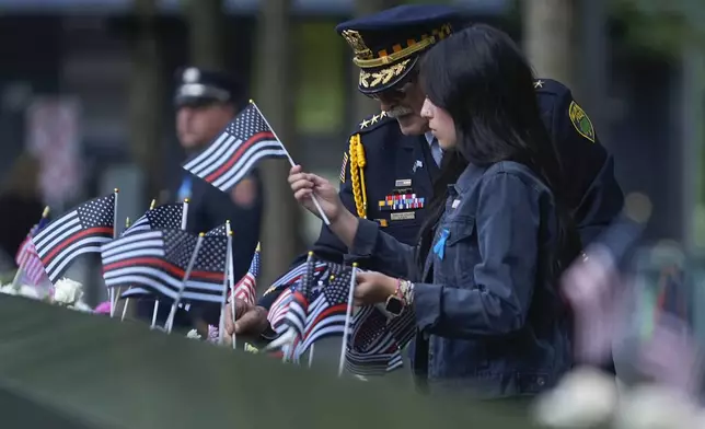 Sam Pulia, left, Willow Springs, Ill police chief, places flags on the bronze parapets at the 9/11 Memorial on the 23rd anniversary of the Sept. 11, 2001 terror attacks, Wednesday, Sept. 11, 2024, in New York. (AP Photo/Pamela Smith)