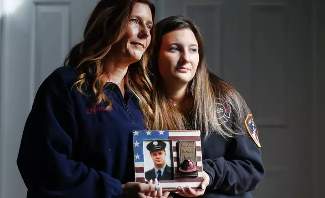 Pamela Yarosz and her daughter Capri are shown with a photo of New York firefighter Christopher Michael Mozzillo Saturday, Sept. 7, 2024, in Freehold, N.J.. Mozzillo, who died in the 9/11 attacks, was Pamela's brother. (AP Photo/Noah K. Murray)