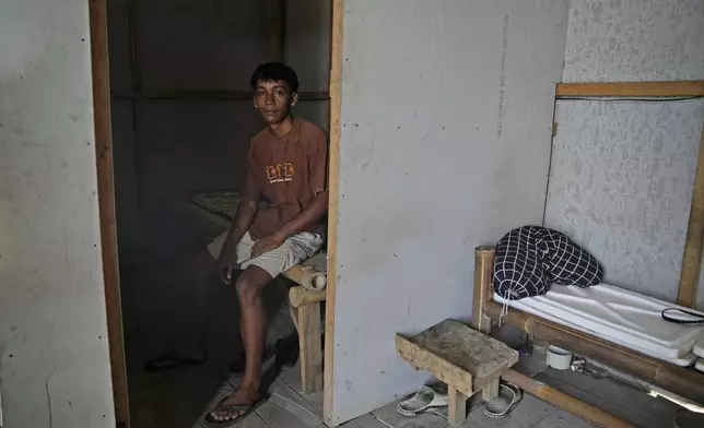 Farm worker Dias Yudho Prihantoro sits on his bed inside the hut where he and his brother stay during their work shifts at a shrimp farm in Kebumen, Central Java, Indonesia, Tuesday, Sept. 24, 2024. (AP Photo/Dita Alangkara)