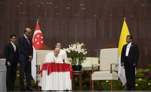 Pope Francis signs the book of honor during a welcome ceremony with the President of the Singapore Republic Tharman Shanmugaratnam, second from left, at the Parliament House in Singapore, Thursday, Sept. 12, 2024. Pope Francis flew to Singapore on Wednesday for the final leg of his trip through Asia, arriving in one of the world's richest countries from one of its poorest after a record-setting final Mass in East Timor. (AP Photo/Gregorio Borgia)