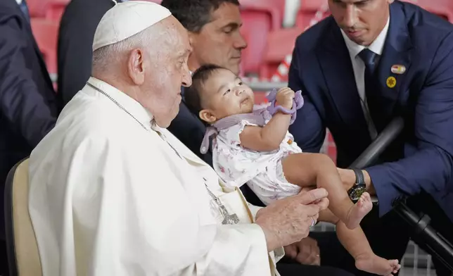 An aide holds a child for Pope Francis' blessings after he arrived to preside a holy mass at the SportsHub National Stadium in Singapore, Thursday, Sept. 12, 2024. (AP Photo/Vincent Thian)