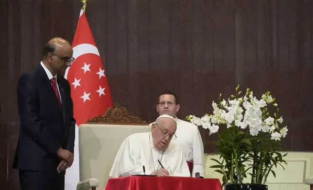 Pope Francis signs the book of honor during a welcome ceremony with the President of the Singapore Republic Tharman Shanmugaratnam, left, at the Parliament House in Singapore, Thursday, Sept. 12, 2024. Pope Francis flew to Singapore on Wednesday for the final leg of his trip through Asia, arriving in one of the world's richest countries from one of its poorest after a record-setting final Mass in East Timor. (AP Photo/Gregorio Borgia)