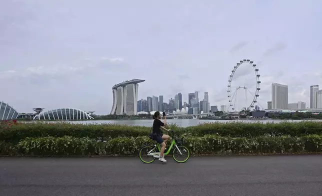 A cyclist takes photo of the city skyline in Singapore, Sunday, Sept. 8, 2024. (AP Photo/Suhaimi Abdullah)