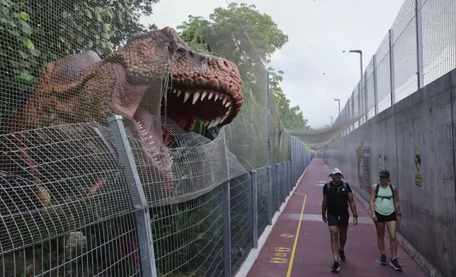 People walk past past a life size dinosaur replica along the Changi Jurassic Mile in Singapore, Sunday, Sept. 8, 2024. (AP Photo/Suhaimi Abdullah)