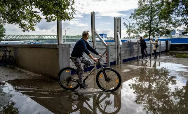 A man riding a bicycle is reflected in water infiltrated through anti-flood barriers on the banks of the River Danube, in Bratislava, Slovakia, Tuesday, Sept. 17, 2024. (AP Photo/Tomas Hrivnak)