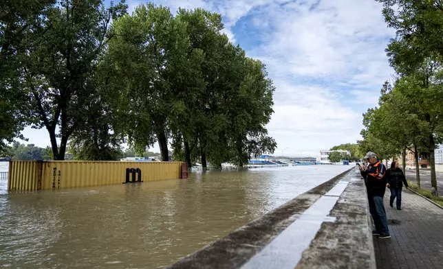 People take photos of rising waters on the banks of the River Danube, in Bratislava, Slovakia, Tuesday, Sept. 17, 2024. (AP Photo/Tomas Hrivnak)