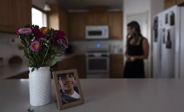 A framed photo of Elijah Ott, who died of a fentanyl overdose at 15, stands next to a vase of flowers as his mother, Mikayla Brown, works in the kitchen in Atascadero, Calif., Friday, Aug. 2, 2024. (AP Photo/Jae C. Hong)