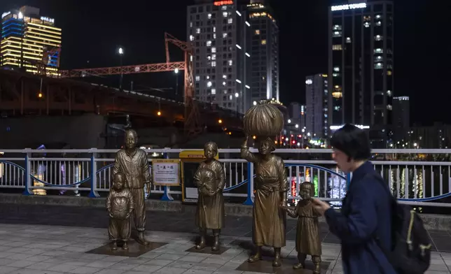 A woman walks past bronze sculptures portraying Korean War refugees in Busan, South Korea, Thursday, May 16, 2024. Busan, the only major city in the country not occupied by North Korean forces during the war, served as a refuge for those fleeing the conflict. (AP Photo/Jae C. Hong)