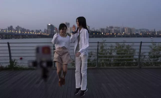 Two tourists jump together as they pose for photos with the Han River in the background at Yeouido Hangang Park, a popular spot for both residents and visitors, as dusk falls over Seoul, Wednesday, May 22, 2024. (AP Photo/Jae C. Hong)