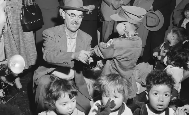 Oregon farmer Harry Holt, left, checks the identification of one of the Korean orphans he brought from South Korea as they arrive in San Francisco, Dec. 17, 1956. (AP Photo/Ernest K. Bennett, File)