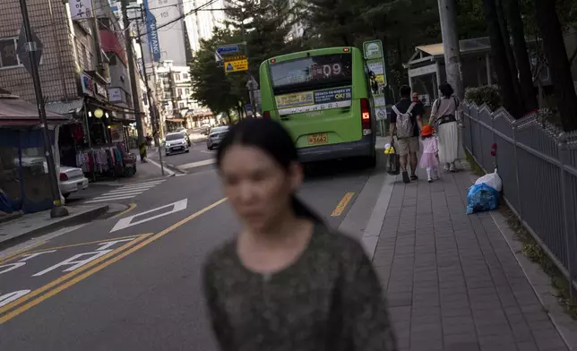 Yooree Kim, foreground, walks along a sidewalk as a family holds hands in the background in Seoul, South Korea, Sunday, May 19, 2024. Kim believes she was robbed of her family when she was sent from South Korea for adoption in France at 11 years old. (AP Photo/Jae C. Hong)