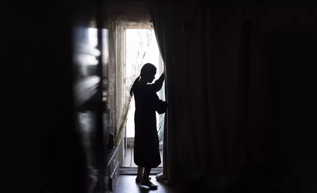 Yooree Kim, who was 11 when she was sent by the Korean adoption agency Holt Children's Services to a couple in France, opens the curtain in her apartment in Seoul, South Korea, Saturday, May 18, 2024. (AP Photo/Jae C. Hong)