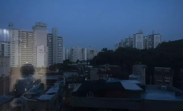 Yooree Kim, who was 11 when she was sent by the Korean adoption agency Holt Children's Services to a couple in France, is reflected in the window of her apartment as dusk settles over her neighborhood in Seoul, South Korea, Saturday, May 18, 2024. (AP Photo/Jae C. Hong)