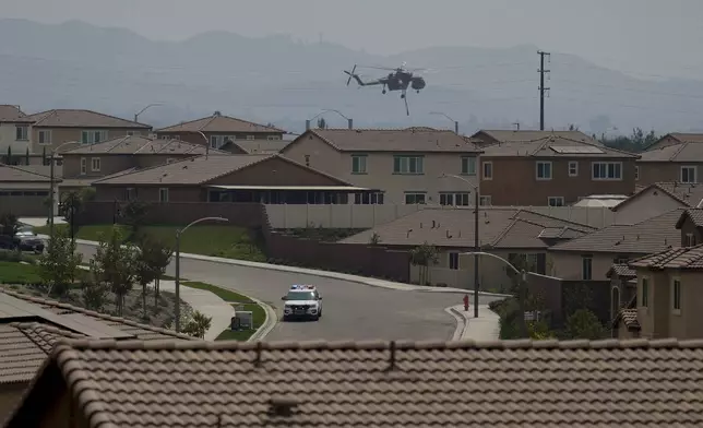 A water dropping helicopter hovers over a neighborhood as crews battle the Line Fire Saturday, Sept. 7, 2024, in Highland, Calif. (AP Photo/Eric Thayer)