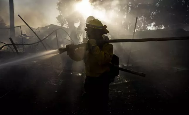 A contract firefighter from Colorado Springs, Colo., douses water on a damaged structure during the Boyles fire in Clearlake, Calif., Sunday, Sept. 8, 2024. (Stephen Lam/San Francisco Chronicle via AP)