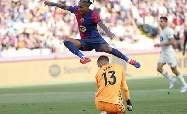 Barcelona's Raphinha, top, jumps over Valladolid's goalkeeper Karl Hein scoring his side's 5th goal during the Spanish La Liga soccer match between FC Barcelona and Valladolid at the Olympic stadium in Barcelona, Spain, Saturday, Aug. 31, 2024. (AP Photo/Joan Monfort)