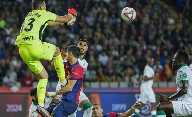Getafe's goalkeeper David Soria, top, makes a save in front of Barcelona's Robert Lewandowski during a Spanish La Liga soccer match between Barcelona and Getafe at the Olympic stadium in Barcelona, Spain, Wednesday, Sept. 25, 2024. (AP Photo/Joan Monfort)