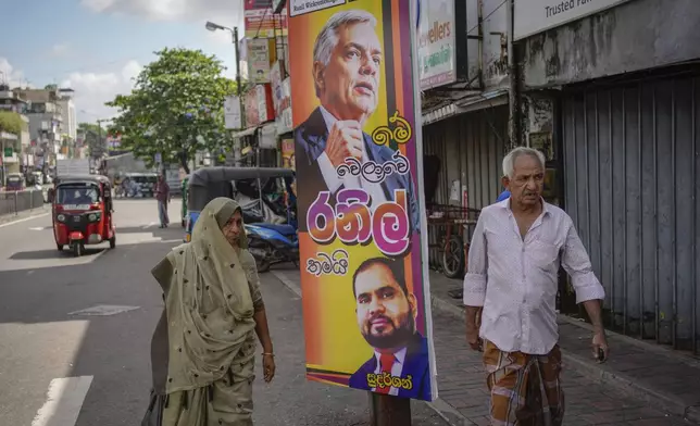 A couple walks past an election poster showing a portrait of Sri Lankan President Ranil Wickremesinghe in Colombo, Sri Lanka, Monday, Sept. 16, 2024. (AP Photo/Eranga Jayawardena)