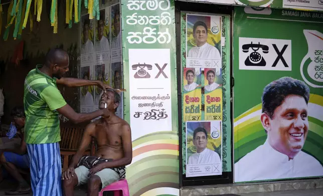 A man sits next to election posters of opposition leader Sajith Premadasa as he gets a shave from a roadside barber in Colombo, Sri Lanka, Tuesday, Sept. 17, 2024. (AP Photo/Rajesh Kumar Singh)