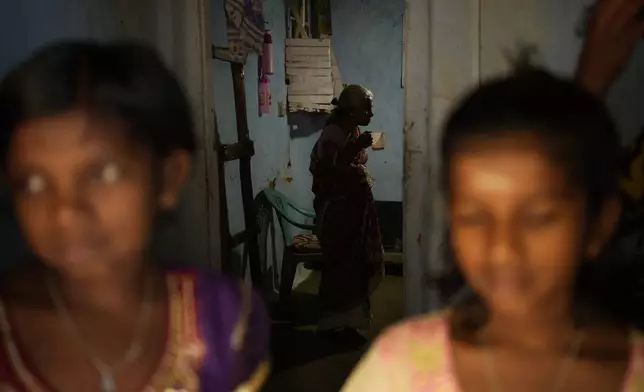 The twin daughters of Muthuthewarkittan Manohari, a tea plantation worker, stand in the foreground as their grandmother Lakshmi, center, drinks a cup of tea in their home in Spring Valley Estate in Badulla, Sri Lanka, Tuesday, Sept. 10, 2024. (AP Photo/Eranga Jayawardena)