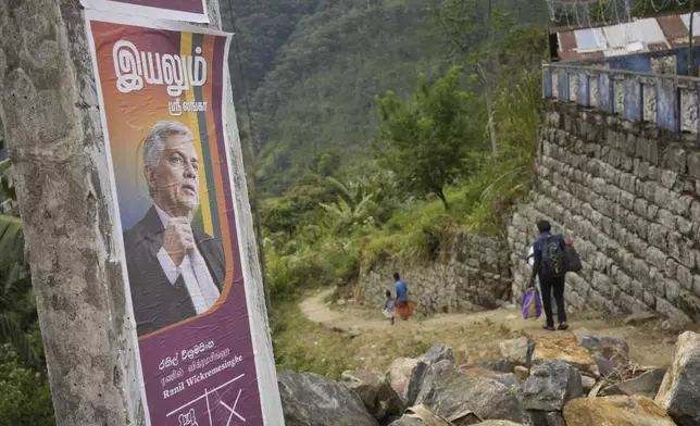 Tea plantation workers at Spring Valley Estate walk past an election poster with a portrait of the Sri Lankan president Ranil Wickremesinghe, ahead of the country's presidential election, in Badulla, Sri Lanka, Monday, Sept. 9, 2024. (AP Photo/Eranga Jayawardena)