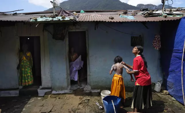 Muthuthewarkittan Manohari, a tea plantation worker, right, bathes her younger daughter Madubhashini, as her elder daughter Shalani, center, stands at the doorway of their small house in Spring Valley Estate in Badulla, Sri Lanka, Monday, Sept. 9, 2024. (AP Photo/Eranga Jayawardena)