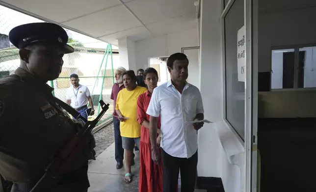 Sri Lankan police officer stands guard as voters queue to cast their vote at a polling center for presidential election in Colombo, Sri Lanka, Saturday, Sept. 21, 2024. (AP Photo/Rajesh Kumar Singh)