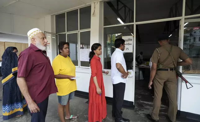 Sri Lankan police officer stands guard as voters queue to cast their vote at a polling center for presidential election in Colombo, Sri Lanka, Saturday, Sept. 21, 2024. (AP Photo/Rajesh Kumar Singh)