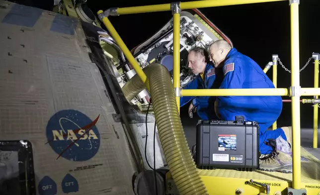 NASA astronauts Mike Fincke, left, and Scott Tingle look inside NASA's Boeing Crew Flight Test Starliner spacecraft after the empty capsule landed at White Sands Missile Range's Space Harbor, Friday, Sept. 6, 2024, in New Mexico. (Aubrey Gemignani/NASA via AP)