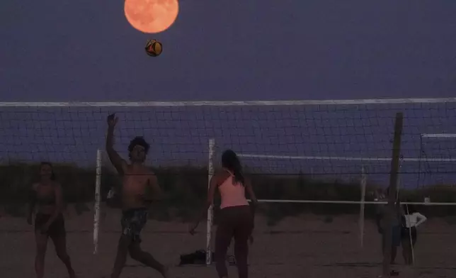 The pumpkin-colored Harvest moon rises over the beach as people play volleyball on the shore of Lake Michigan in Chicago, Tuesday, Sept. 17, 2024. (AP Photo/Kiichiro Sato)