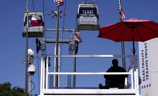 A Dallas police officer, sitting bottom right, watches activity from a high platform as sky cabs make their way past at the State Fair of Texas in Dallas, Friday, Sept. 27, 2024. (AP Photo/Tony Gutierrez)