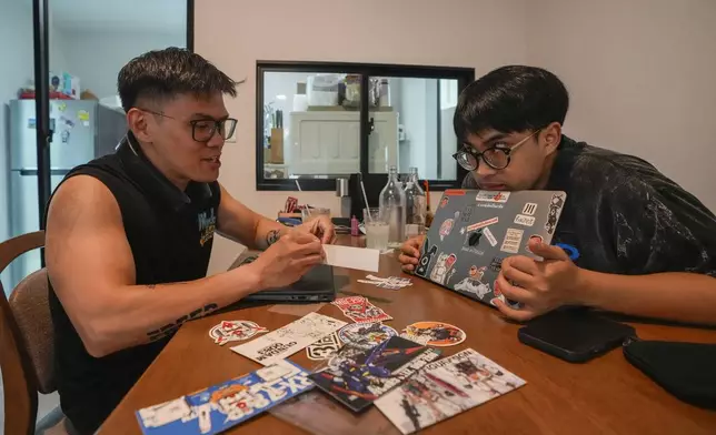 Kunchanok Khantiphong, 27, watches his Filipino partner Edward Jonathan Caiga, 42, put stickers on his computer at home in Bangkok, Thailand, Saturday, July 6, 2024. (AP Photo/Sakchai Lalit)