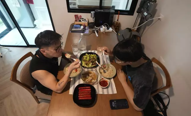 Kunchanok khantiphong, 27, right, and his Filipino partner Edward Jonathan Caiga, 42, eat lunch at home in Bangkok, Thailand, Saturday, July 6, 2024. (AP Photo/Sakchai Lalit)