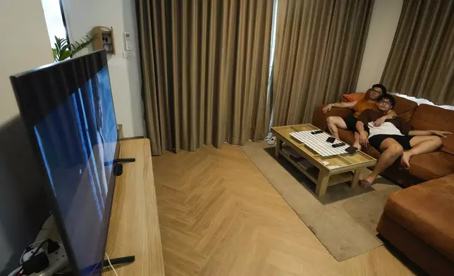 Edward Jonathan Caiga, 42, left, and his partner Kunchanok Khantiphong, 27, watch television at home in Bangkok, Thailand, Saturday, July 6, 2024. (AP Photo/Sakchai Lalit)