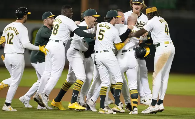 Oakland Athletics players surround Seth Brown as they celebrate his game-winning single during the 13th inning against the Detroit Tigers in a baseball game Friday, Sept. 6, 2024, in Oakland, Calif. Oakland won 7-6. (AP Photo/Tony Avelar)