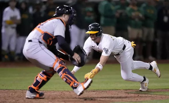 Oakland Athletics' Max Schuemann (12) slides into home plate past Detroit Tigers catcher Jake Rogers (34) to score a run on a sacrifice hit by Brent Rooker during the 12th inning of a baseball game Friday, Sept. 6, 2024, in Oakland, Calif. (AP Photo/Tony Avelar)