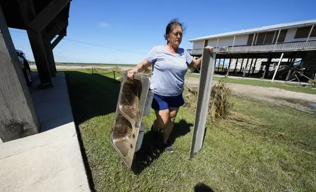 Natalie Bergeron, a letter carrier who has been delivering mail on this route for 43 years, helps a customer clean up debris who took damage from Hurricane Francine, in Cocodrie, La., Thursday, Sept. 12, 2024. (AP Photo/Gerald Herbert)