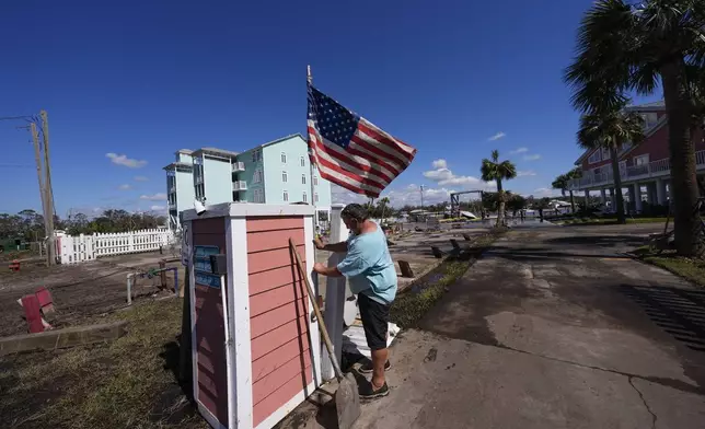 Daniel Dickert plants an American flag on is property were his boat shed was destroyed and his home damaged in the aftermath of Hurricane Helene, in Jena, Fla., Sunday, Sept. 29, 2024. (AP Photo/Gerald Herbert)