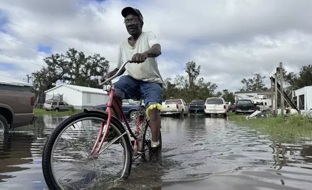 Carter Caldwell bikes through his family's flooded property just south of Houma, La. after Hurricane Francine tore through the area, Thursday, Sept. 12, 2024. (AP Photo/Jack Brook)