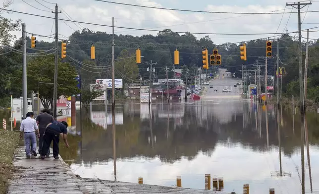 A passerby checks the water depth of a flooded road, Saturday, Sept. 28, 2024, in Morganton, N.C. Torrential rain from Hurricane Helene left many area streets flooded. In addition, traffic lights are inoperable due to no power, with downed power lines and trees. (AP Photo/Kathy Kmonicek)