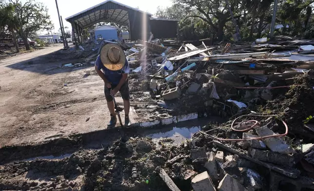 Chris Jordan, maintenance manager for Horseshoe Beach, tries to find a water shutoff valve amid the rubble of the destroyed city hall in the aftermath of Hurricane Helene, in Horseshoe Beach, Fla., Sunday, Sept. 29, 2024. (AP Photo/Gerald Herbert)