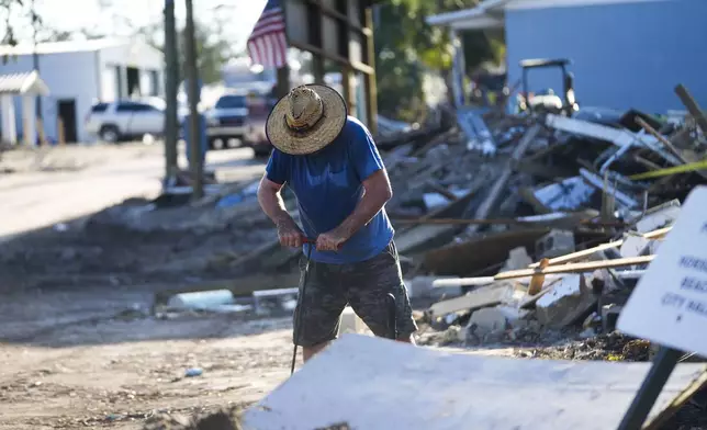 Chris Jordan, maintenance manager for Horseshoe Beach, tries to find a water shutoff valve amid the rubble of the destroyed city hall in the aftermath of Hurricane Helene, in Horseshoe Beach, Fla., Sunday, Sept. 29, 2024. (AP Photo/Gerald Herbert)