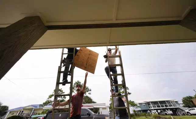 Jerry McCullen, top of ladder left, and Carson Baze, top of ladder right, put plywood over the windows of a house ahead of Hurricane Helene, expected to make landfall Thursday evening, in Alligator Point, Fla., Wednesday, Sept. 25, 2024. (AP Photo/Gerald Herbert)