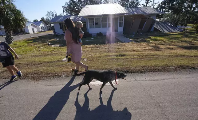 A loose dog walks past a group from St. Augustine, Fla., who did not want to give their name, that arrived to help storm victims, as they walk to pray outside the damaged First Baptist Church in the aftermath of Hurricane Helene, in Horseshoe Beach, Fla., Sunday, Sept. 29, 2024. (AP Photo/Gerald Herbert)